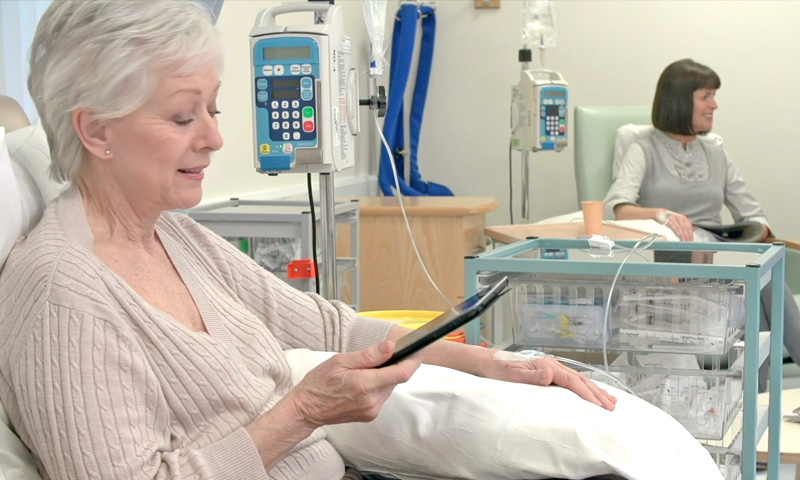 A woman is reading on her tablet while receiving chemo treatment