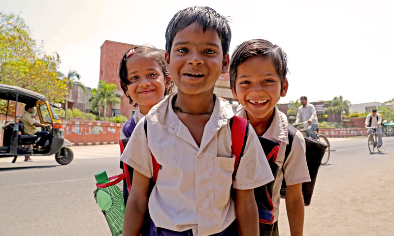 Three children pose in front of a school in India